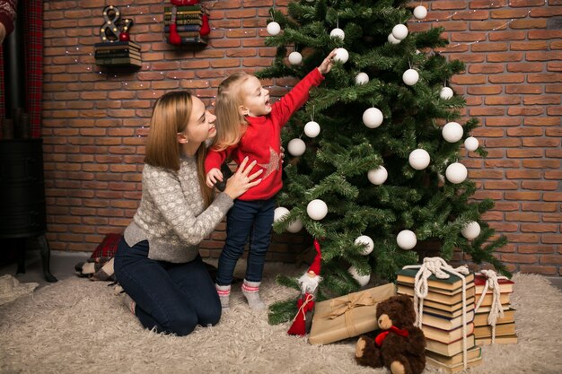 Madre e hija colgando juguetes en un árbol de Navidad