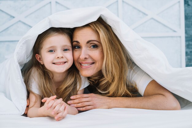 Madre e hija felices bajo una manta blanca