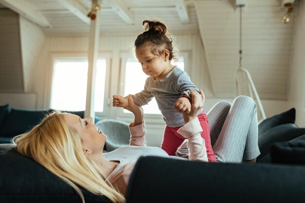 Madre e hija juguetonas divirtiéndose juntas en casa. El foco está en la niña.