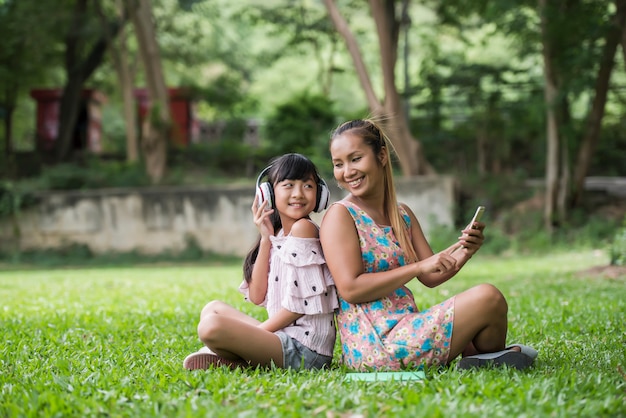 Madre e hija leyendo un cuento de hadas a su hija escuchar sonido con auriculares en el parque