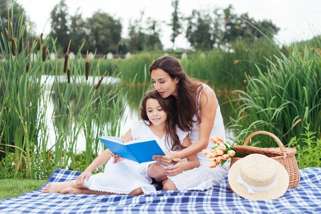 Madre e hija leyendo un libro junto al lago