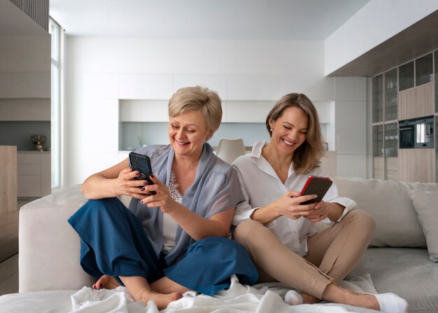 Madre e hija leyendo mensajes en teléfonos inteligentes juntos en casa en el sofá