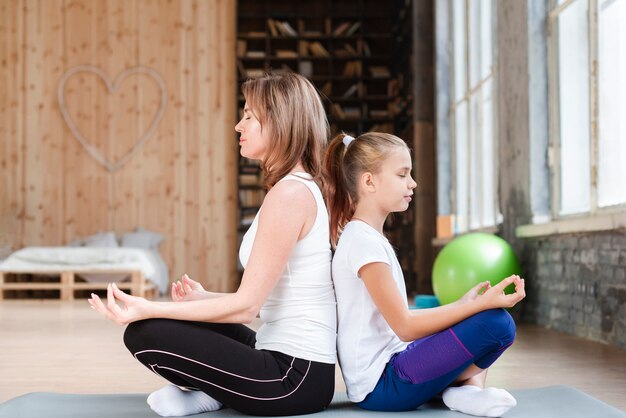 Madre e hija meditando espalda con espalda