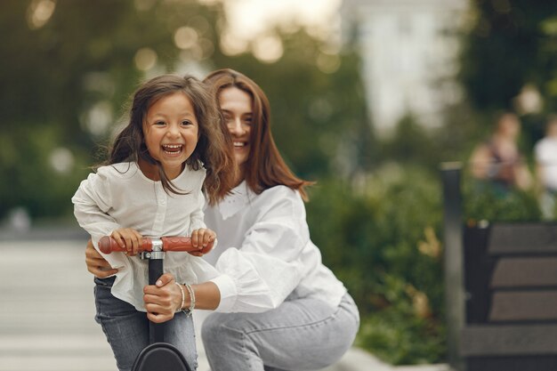 Madre e hija en patinete en el parque. Los niños aprenden a patinar. Niña patinando en un día soleado de verano.