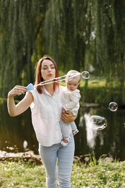 Madre e hija pequeña descansando en el parque y posando para una foto. Familia vistiendo ropa blanca y azul claro