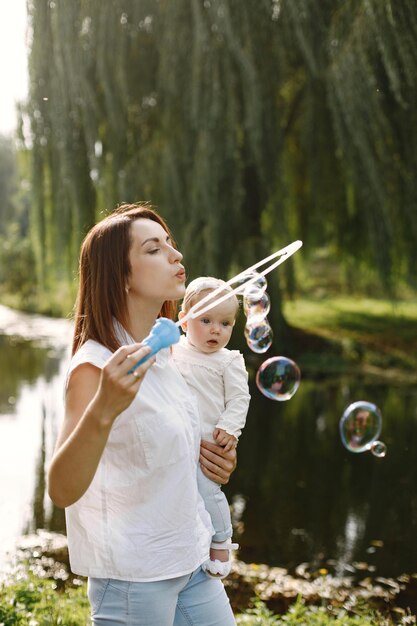 Madre e hija pequeña descansando en el parque y posando para una foto. Familia vistiendo ropa blanca y azul claro