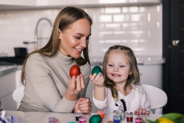 Madre e hija pequeña con huevos de pascua y canasta de pascua en la cocina lista para Pascua