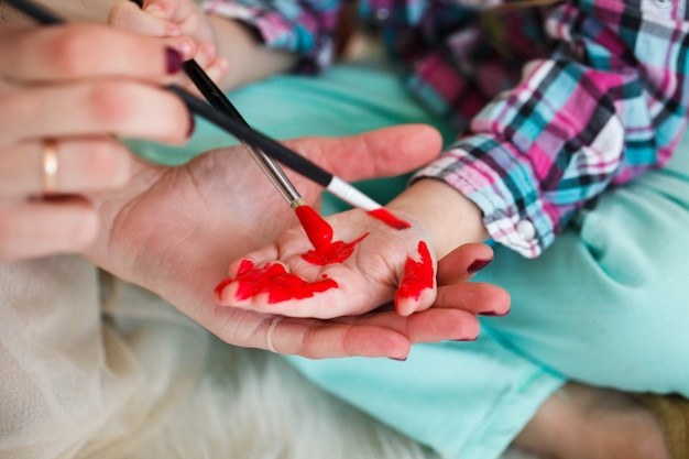 Madre e hija pintan sus manos en color rojo sentado en el suelo