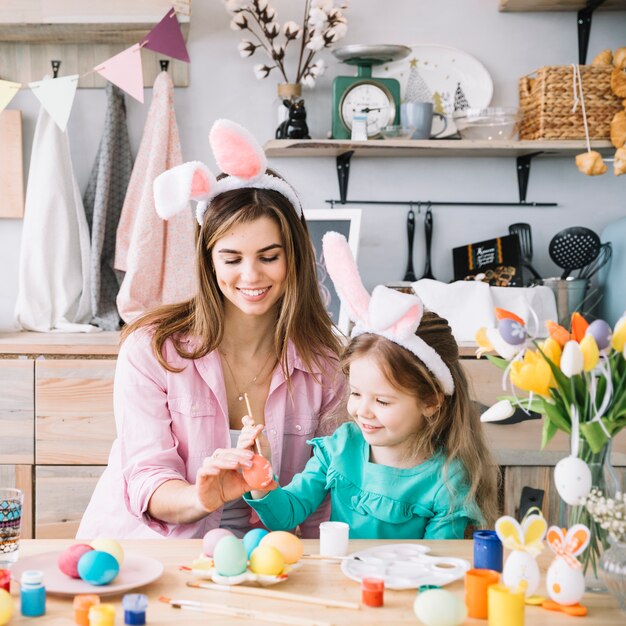 Madre e hija pintando huevos para Pascua en mesa