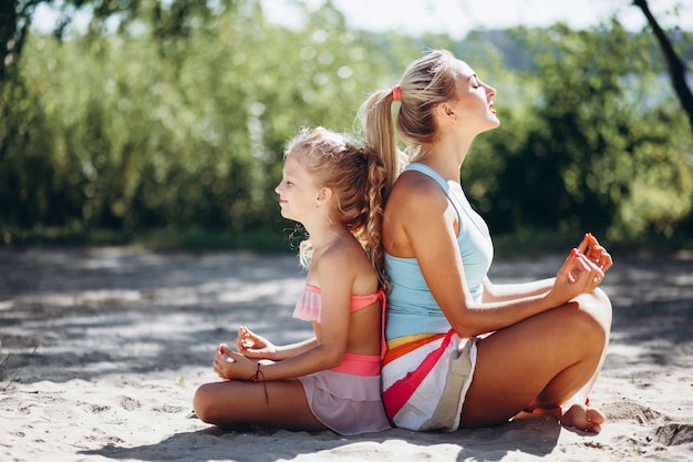 Madre e hija en la playa practicando yoga