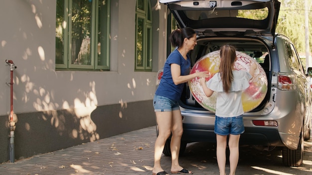 Foto gratuita madre e hija poniendo equipaje en el maletero del camión mientras disfrutan de un viaje de vacaciones. mujer y niña cargando vehículos con equipaje mientras se preparan para vacaciones en la ciudad.