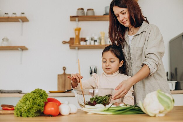 Madre e hija preparando ensalada cocinando en la cocina