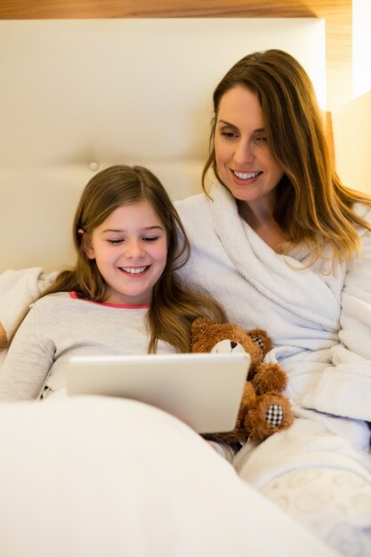 Madre e hija que usa la tableta digital en el dormitorio