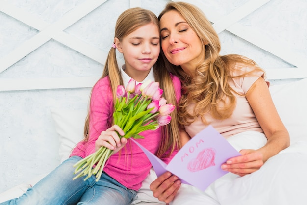 Foto gratuita madre e hija sentada con flores y tarjeta de felicitación