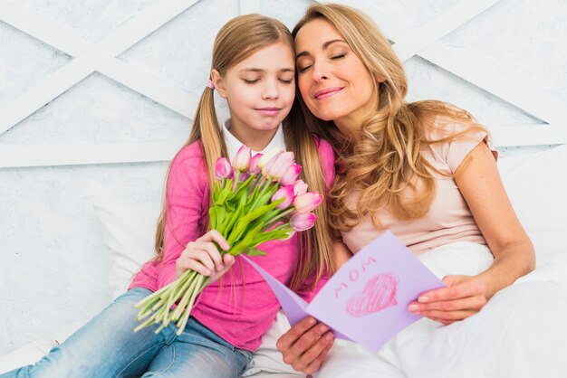 Madre e hija sentada con flores y tarjeta de felicitación