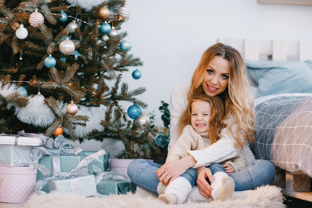 madre e hija sentada junto al árbol de navidad