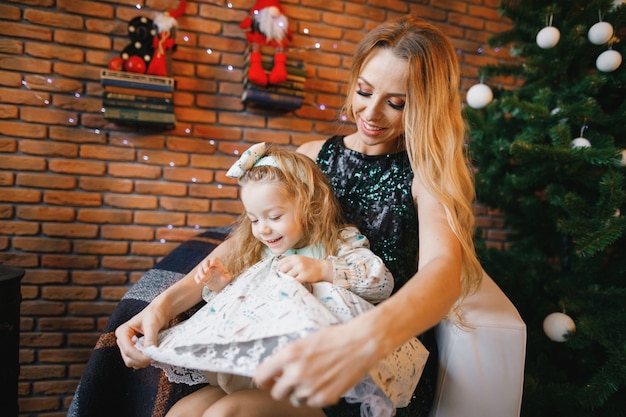 madre e hija sentada junto al árbol de navidad