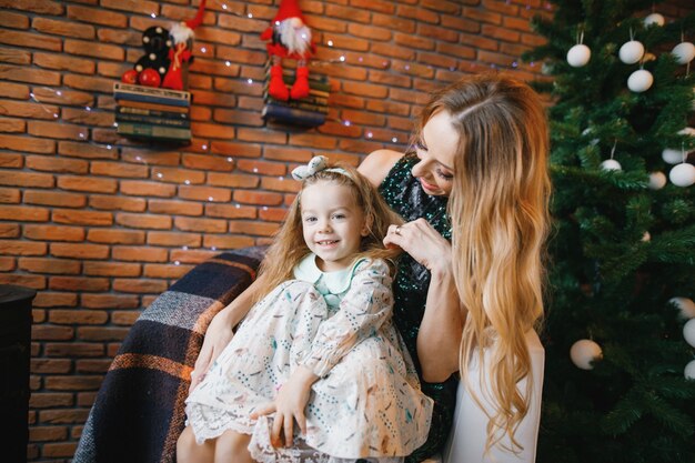 madre e hija sentada junto al árbol de navidad