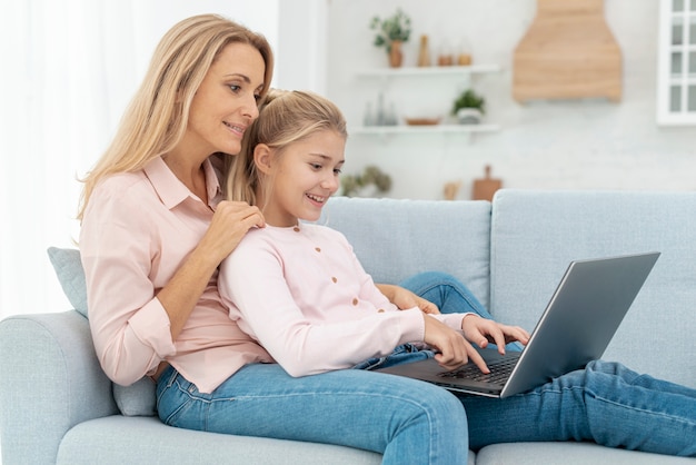 Madre e hija sentada en el sofá y trabajando en la computadora portátil
