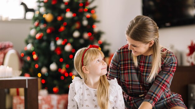 Madre e hija sentadas enfrente de árbol de navidad