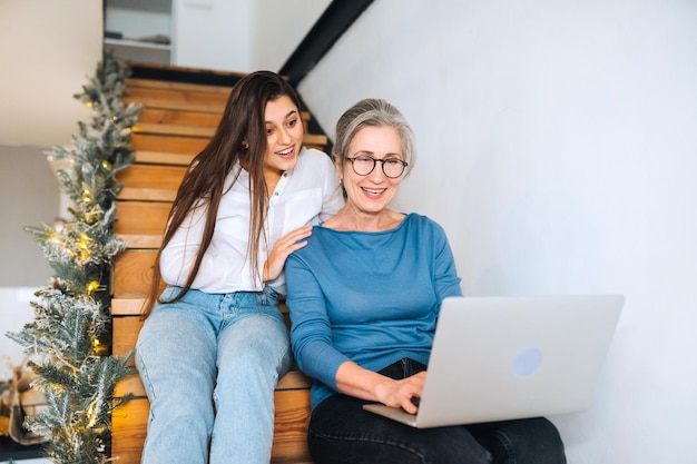 Madre e hija sentadas en los escalones y viendo algo en la computadora portátil