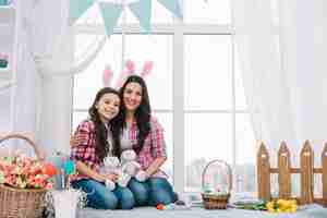 Foto gratuita madre e hija sentadas juntas sosteniendo un conejito de peluche en la celebración de pascua