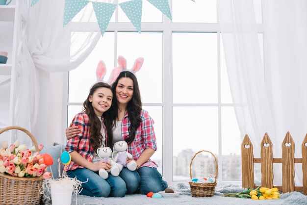 Madre e hija sentadas juntas sosteniendo un conejito de peluche en la celebración de Pascua