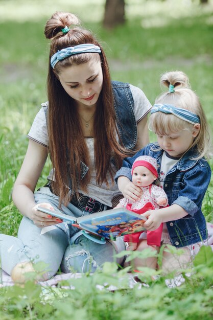 Madre e hija sentadas en el suelo leyendo un libro y la niña con una muñeca