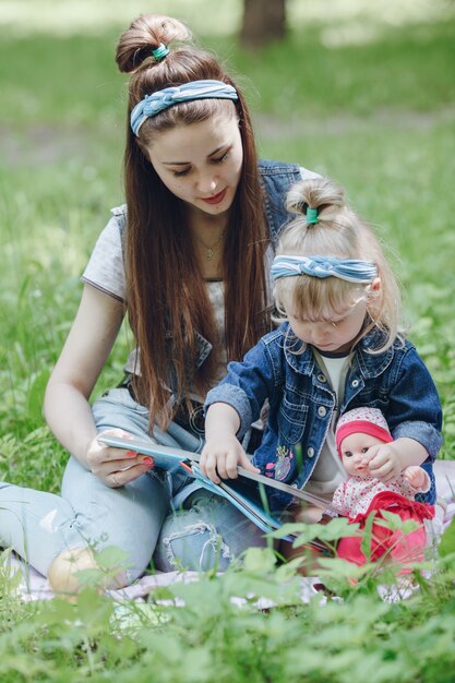 Madre e hija sentadas en el suelo leyendo un libro y la niña con una muñeca