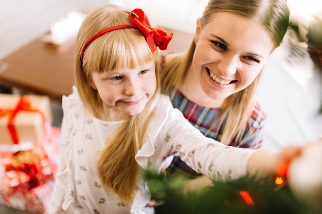 Madre e hija sonrientes decorando árbol de navidad juntas