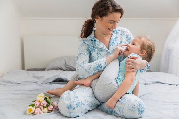 Madre e hija sonrientes que juegan en cama