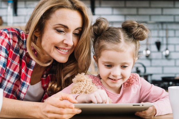 Madre e hija sonrientes que usan la tableta digital en cocina