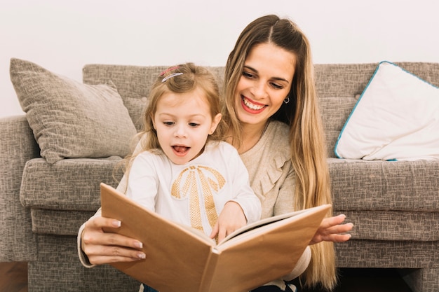 Madre e hija sorprendida leyendo el libro cerca del sofá