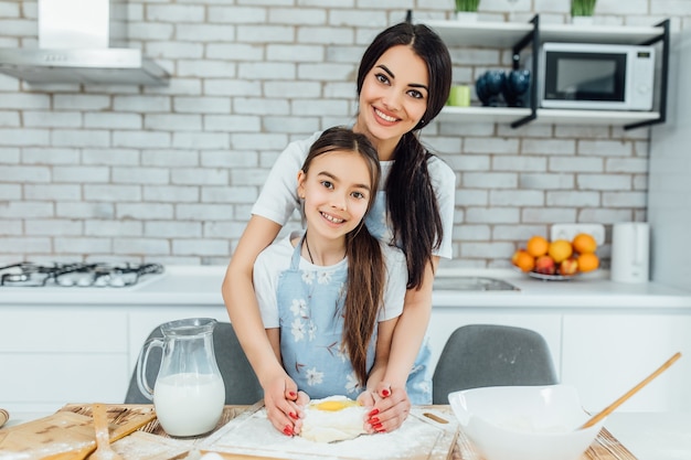 Madre e hija sosteniendo la bandeja con galletas sin hornear juntos en la cocina