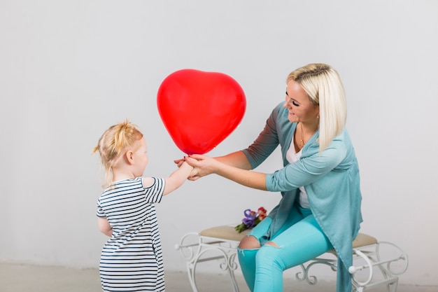 Madre e hija sosteniendo corazón rojo globo