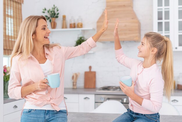 Madre e hija sosteniendo tazas y saludando