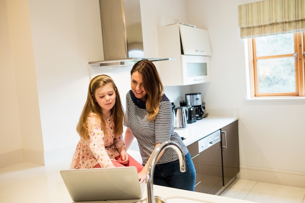 Madre e hija usando la computadora portátil en la cocina