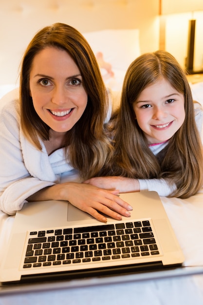 Madre e hija usando la computadora portátil en dormitorio