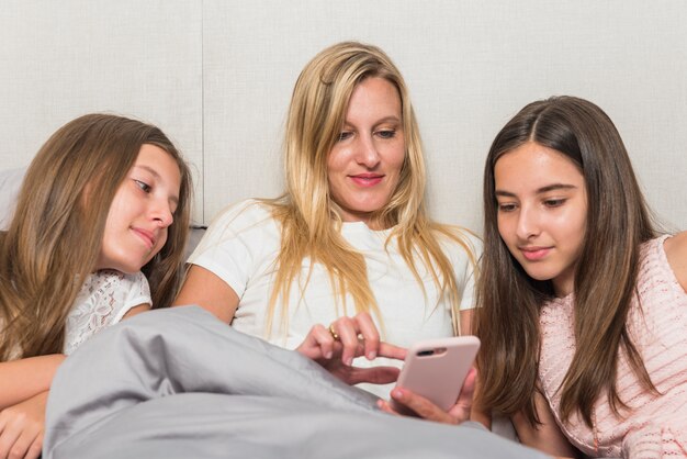Madre e hijas sentada con teléfono inteligente en la cama