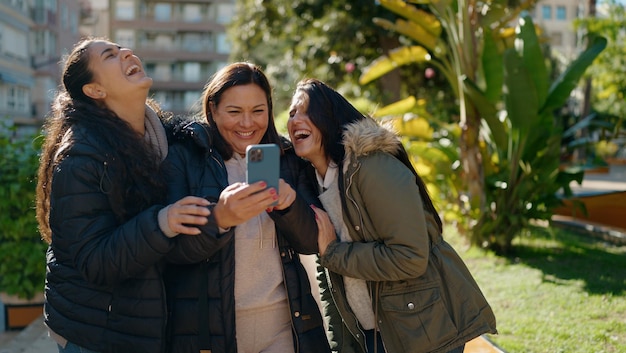 Madre e hijas usando un teléfono inteligente parados juntos en el parque