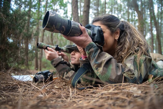 Madre e hijo absortos tomando fotos en el bosque. Familia con cámaras modernas tiradas en el suelo, usando cámara y binoculares. Crianza, familia, concepto de ocio.