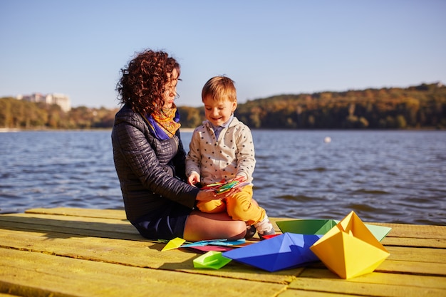 Madre e hijo jugando con barquitos de papel junto al lago