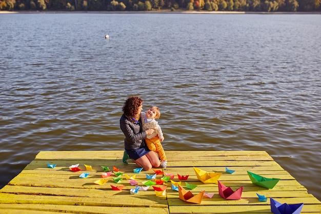 Madre e hijo jugando con barquitos de papel junto al lago