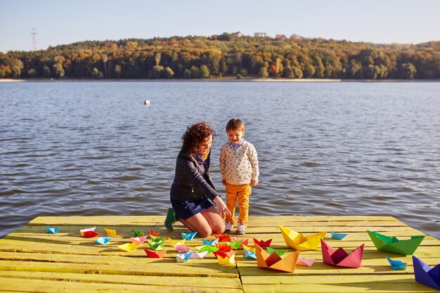 Madre e hijo jugando con barquitos de papel junto al lago