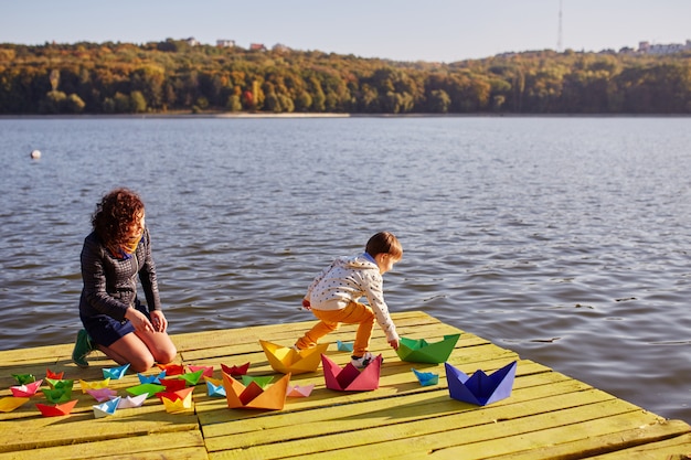 Foto gratuita madre e hijo jugando con barquitos de papel junto al lago