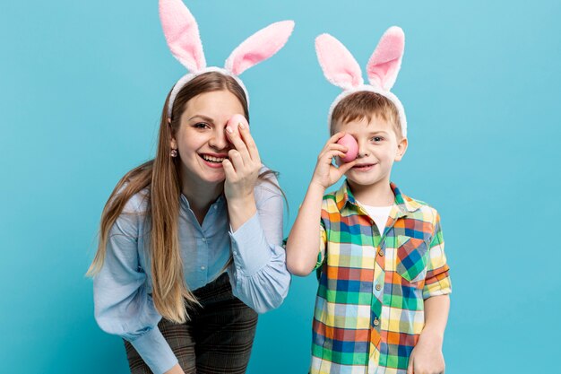 Madre e hijo con orejas de conejo que cubren los ojos con huevos pintados