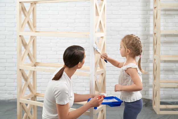 Madre e hijo pintando estante de madera en casa