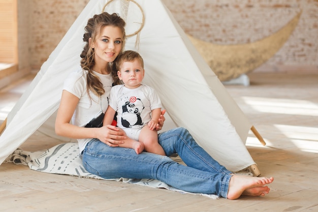 Madre e hijo sentados posando cerca de la tienda de campaña en loft estudio con fondo de pared de ladrillo