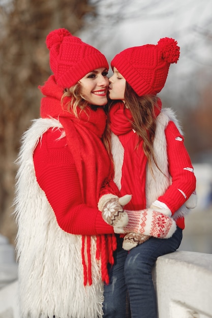 Madre e hijo con sombreros de invierno tejidos en vacaciones familiares de Navidad. Gorro y bufanda de lana hechos a mano para mamá y niño. Tejer para niños. Prendas de abrigo de punto. Mujer y niña en un parque.