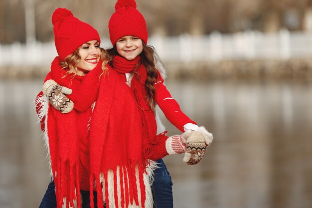 Madre e hijo con sombreros de invierno tejidos en vacaciones familiares de Navidad. Gorro y bufanda de lana hechos a mano para mamá y niño. Tejer para niños. Prendas de abrigo de punto. Mujer y niña en un parque.